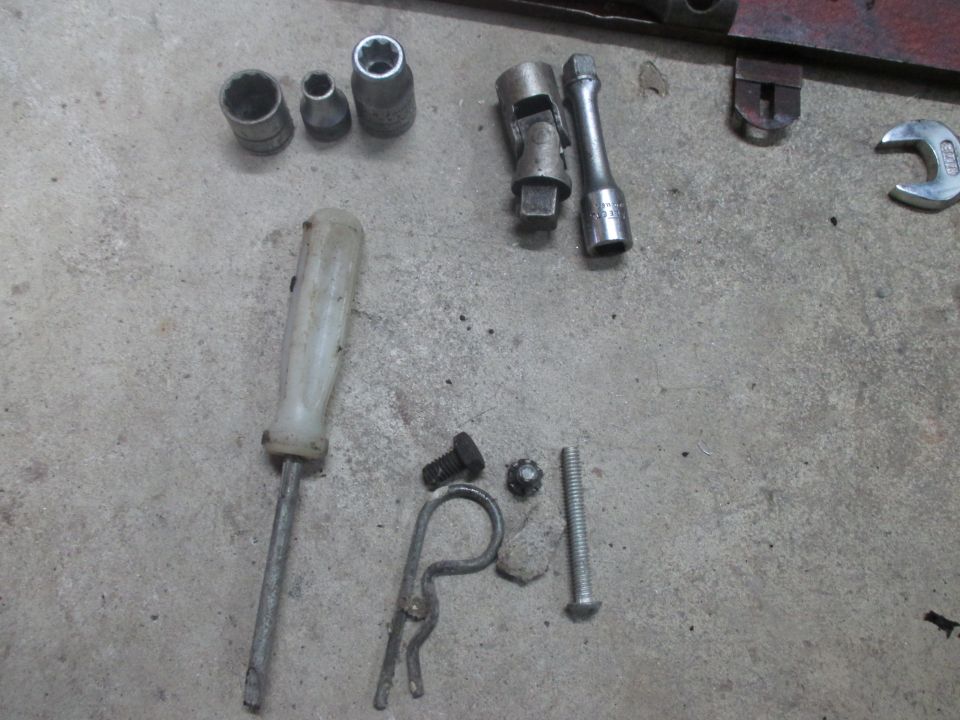 Screwdriver, socket wrenches, bolts, and a cotter pin on a concrete surface