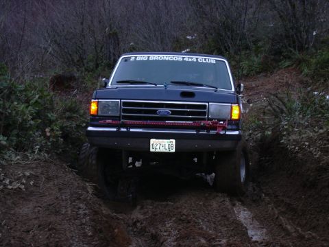 1991 Ford Bronco - This Ford Bronco is navigating a muddy trail, with a club sticker visible on its windshield.