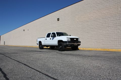 2006 Chevrolet Silverado 2500 - A white 2006 Chevrolet Silverado 2500 pickup truck is parked on asphalt in front of a large beige brick building.