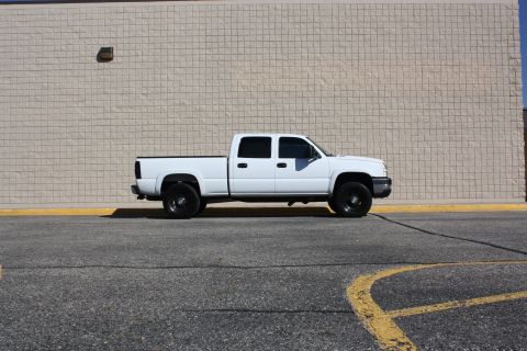 2006 Chevrolet Silverado 2500 - Side view of a white pickup truck with black rims parked in front of a beige brick wall.