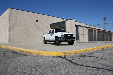 2006 Chevrolet Silverado 2500 - A white 2006 Chevrolet Silverado 2500 pickup truck is parked outside a commercial building under a clear blue sky.