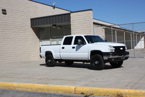 2006 Chevrolet Silverado 2500 - A white 2006 Chevrolet Silverado 2500 pickup truck is parked in front of a building with a chain-link fence in the background.