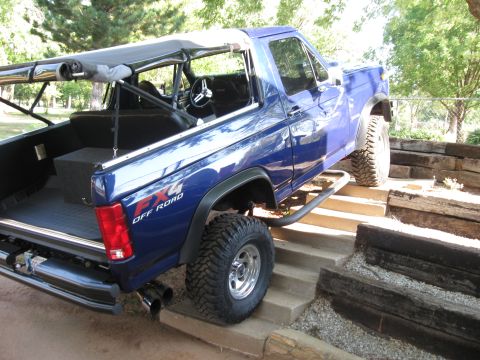 1982 Ford Bronco - This blue 4x4 SUV features a custom roll cage and soft top, seen climbing concrete steps.