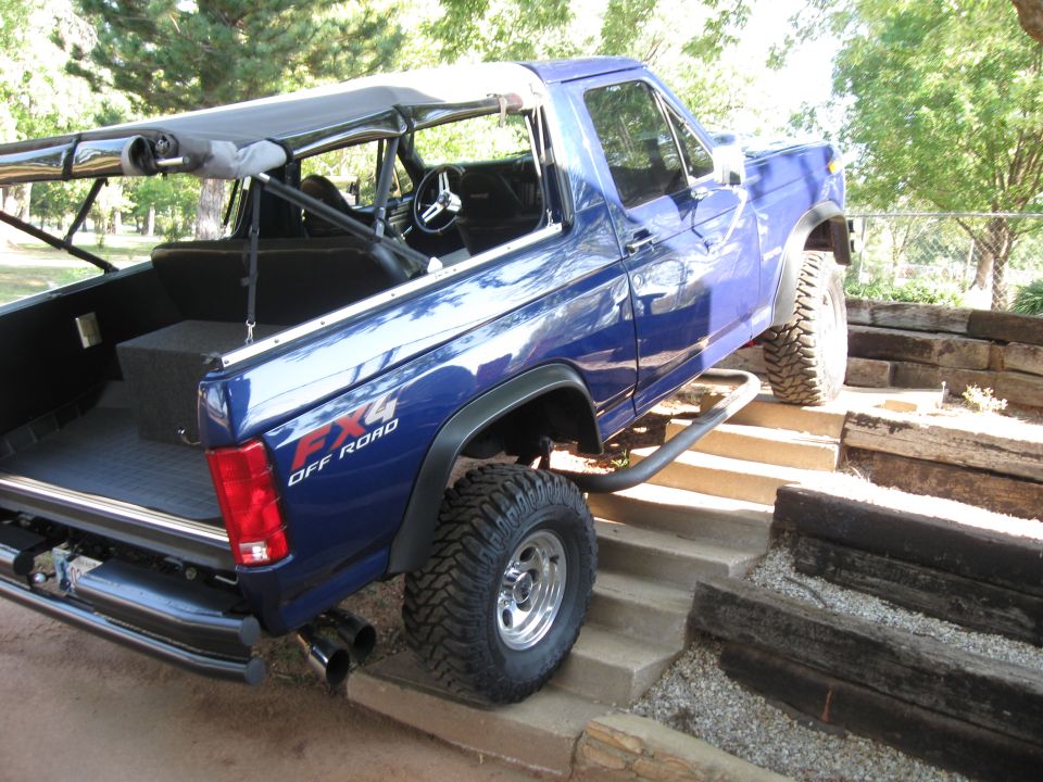 Blue 4x4 off-road SUV with custom roll cage and soft top, climbing concrete steps