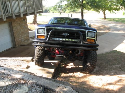 1982 Ford Bronco - Front view of a lifted blue Ford Bronco with a bull bar and LED light bar, parked in a driveway.