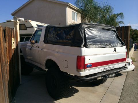 1990 Ford Bronco - Rear view of a lifted 1990 Ford Bronco a black soft top and custom bumper with a website decal.