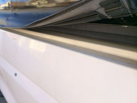 1990 Ford Bronco - Close-up detail of a black vinyl soft-top edge resting against the chrome trim and white painted body panel of a vehicle.