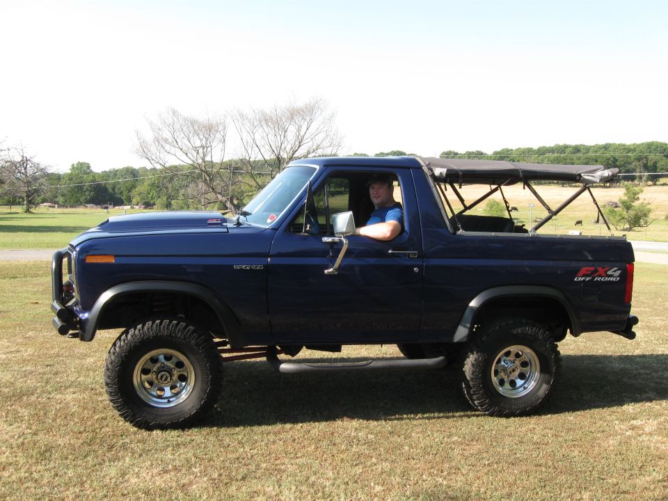 Dark blue Ford Bronco with a soft top, lifted suspension, and off-road tires parked on grass