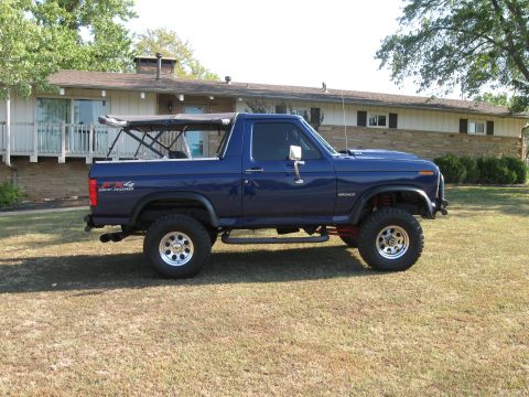 1982 Ford Bronco - A blue Ford Bronco with a soft top is parked on a grassy lawn in front of a house.
