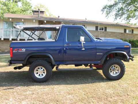 1982 Ford Bronco - This blue Ford Bronco is shown from the side, parked on a grassy lawn in front of a house.