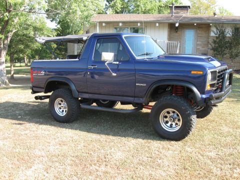 1982 Ford Bronco - This lifted 1982 Ford Bronco features a blue exterior and a removable soft top, parked on a grassy lawn.