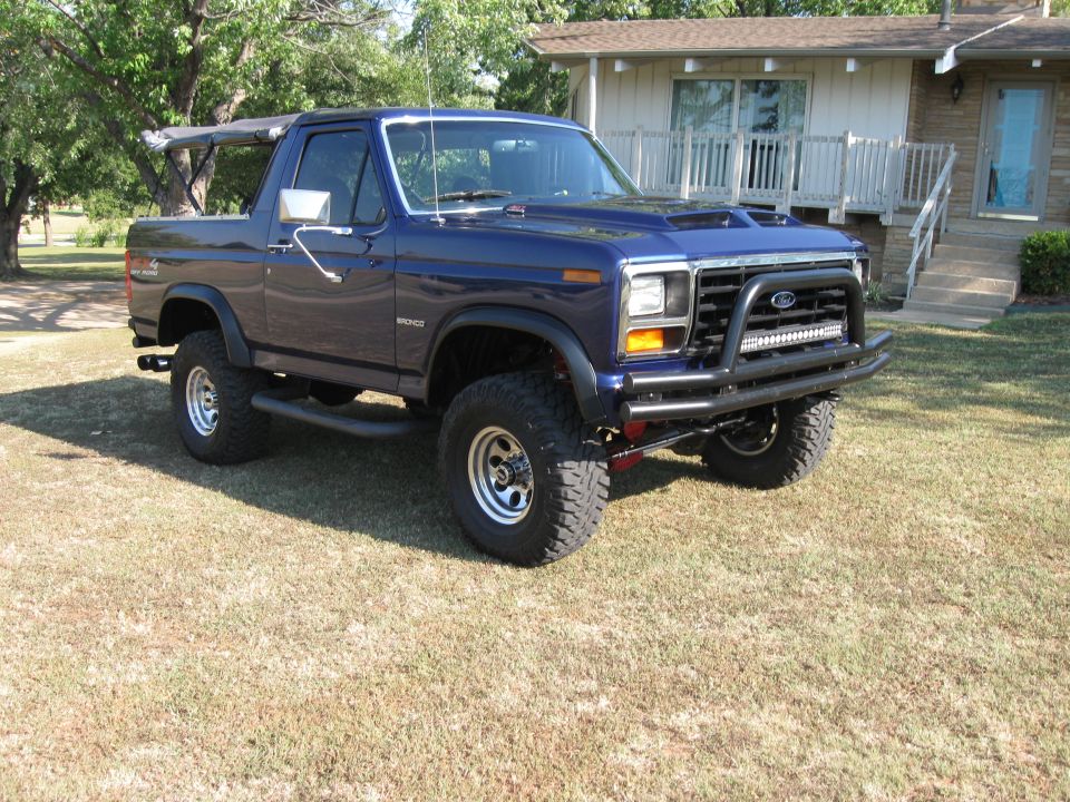 1982 Ford Bronco parked on grass in front of a house, with a custom bull bar and LED light bar