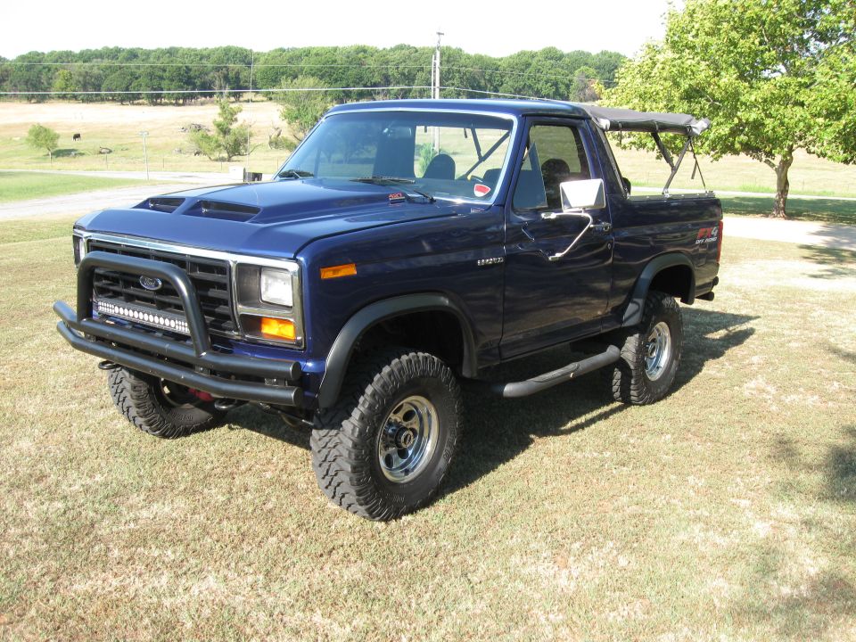 Dark blue Ford Bronco with aftermarket hood scoop and bull bar, parked on grass