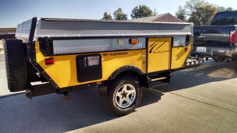 1985 Jeep CJ7 - A yellow Fleetwood Evolution pop-up camper trailer is seen from the side, hitched to a black pickup truck.