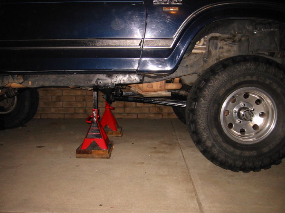 Dark blue Bronco on red jack stands showing underside suspension and large off-road tire