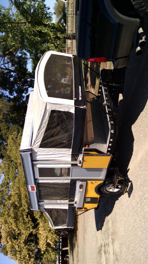 1985 Jeep CJ7 - A pop-up camper trailer is attached to the rear of a pickup truck, parked outdoors.