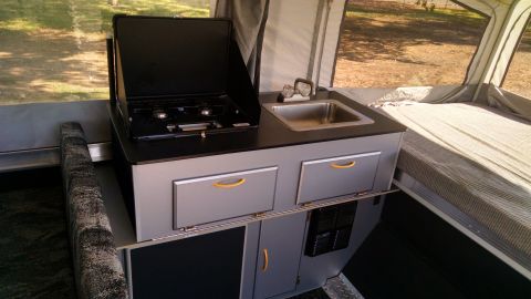 1985 Jeep CJ7 - Interior view of a pop-up camper, showing the kitchen area with a sink and stove, and a bed.
