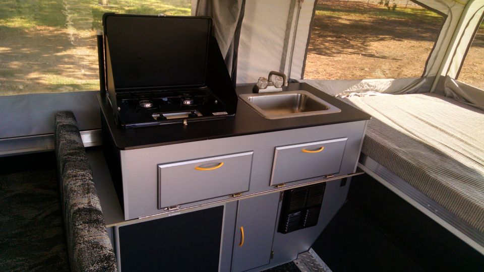 Pop-up camper interior with sink, stove, and bed