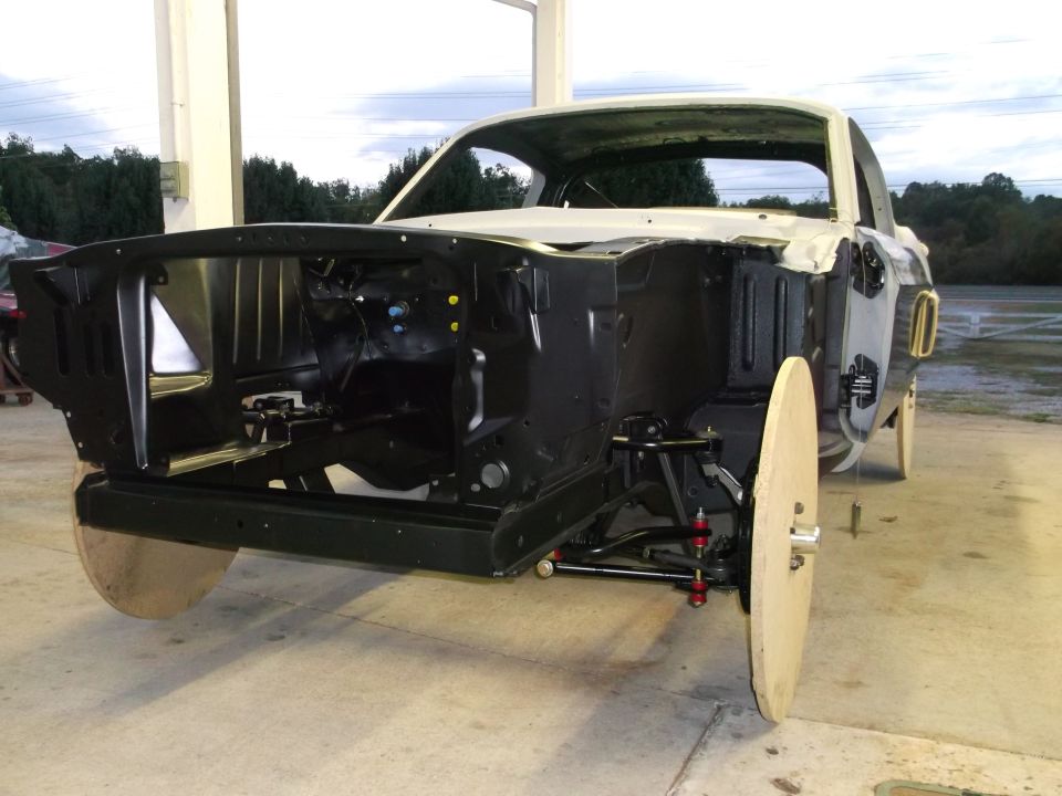 1967 Ford Mustang body in white, front view, undergoing restoration with exposed engine bay and wooden wheel covers