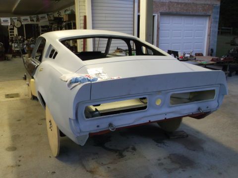 1967 Ford Mustang - The rear of a car body, in primer, is shown in a garage setting, likely undergoing restoration.