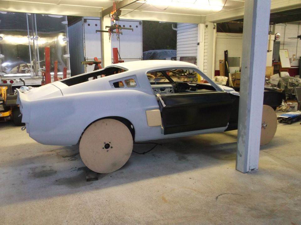Unfinished 1967 Ford Mustang body, primer gray, with wooden wheels, driver's door open