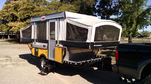 1985 Jeep CJ7 - Pop-up camper trailer with yellow accents is hitched to a black pickup truck.