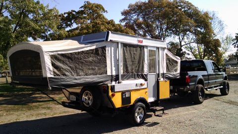 1985 Jeep CJ7 - A dark-colored pickup truck is hitched to a pop-up camper trailer, parked outdoors.