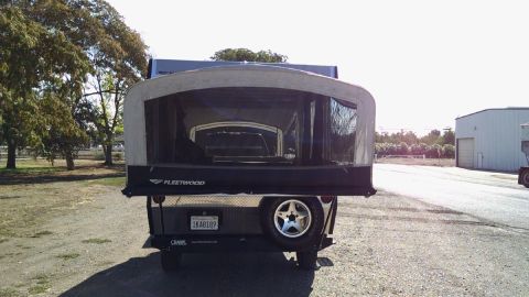 1985 Jeep CJ7 - A pop-up camper trailer is parked outdoors, showing its rear with a spare tire and Fleetwood branding.