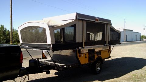 1985 Jeep CJ7 - This pop-up camper trailer is hitched to a truck and parked in an outdoor lot.