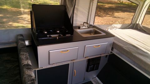 1985 Jeep CJ7 - Interior view of a pop-up camper, showing the kitchen unit with a two-burner stove and sink, adjacent to a sleeping area.