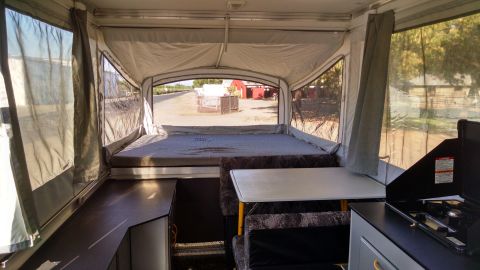 1985 Jeep CJ7 - This pop-up camper interior features a sleeping area, a dinette, and a compact kitchen with a stove.