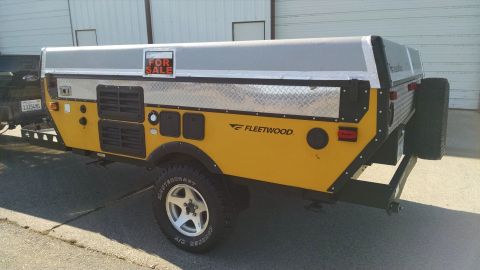 1985 Jeep CJ7 - A Fleetwood camper trailer is parked outside a building, with a 'For Sale' sign visible on its roof.