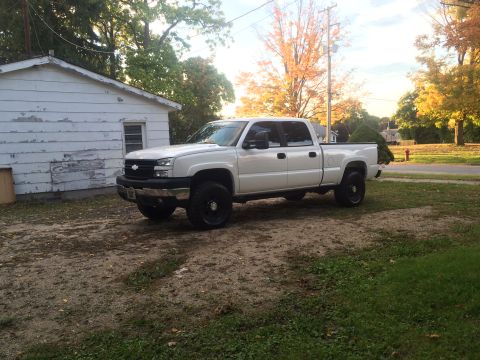 2006 Chevrolet Silverado 2500 - A white 2006 Chevrolet Silverado 2500 pickup truck is parked in a yard with a white shed nearby. The truck has black rims and a crew cab.