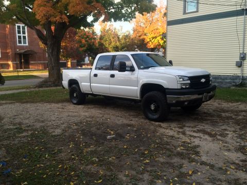 2006 Chevrolet Silverado 2500 - A white Chevrolet Silverado pickup truck is parked on a gravel lot with autumn foliage in the background.