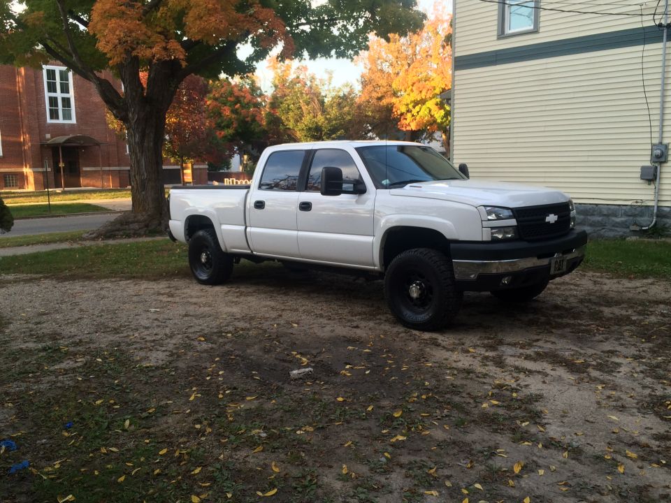 White Chevrolet Silverado pickup truck, 3/4 front view, parked on gravel with autumn leaves