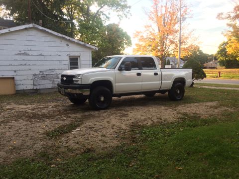 2006 Chevrolet Silverado 2500 - This white 2006 Chevrolet Silverado 2500 pickup truck is seen from a three-quarter front view, parked in a grassy area next to a building.