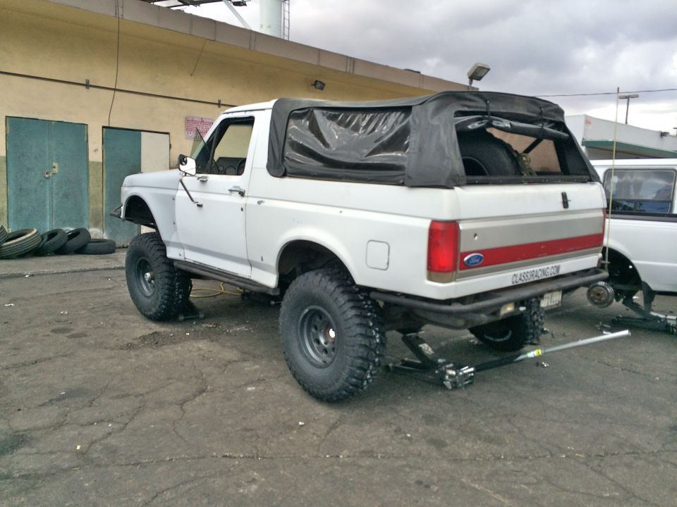 Rear of white lifted Ford SUV with black soft top in an industrial yard
