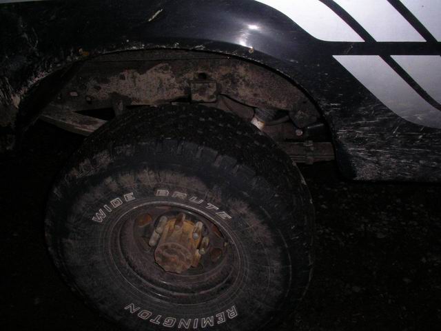Black 1990 Ford F-150 truck wheel and fender, covered in mud. White stripe graphics on fender