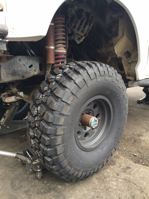 1990 Ford Bronco - Close-up of an off-road tire mounted on a hub with exposed coil-spring suspension under a white lifted truck.