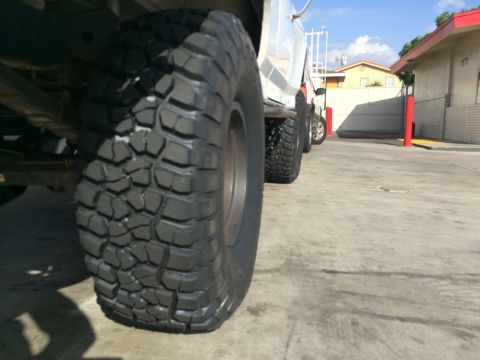 1990 Ford Bronco - Low ground-level view of a deep-lugged off-road tire under a white lifted vehicle in a paved lot.