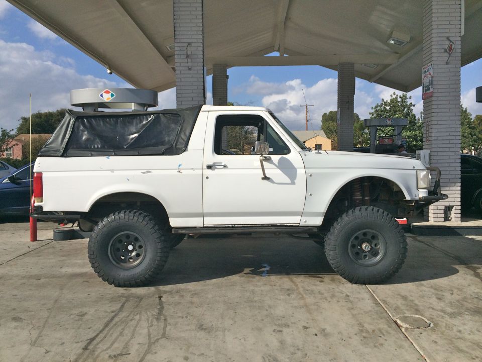 White lifted Ford SUV with black soft top at a gas station