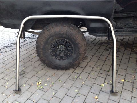 1979 Ford Bronco - A chrome roll cage is positioned in front of a large off-road tire on a black SUV.