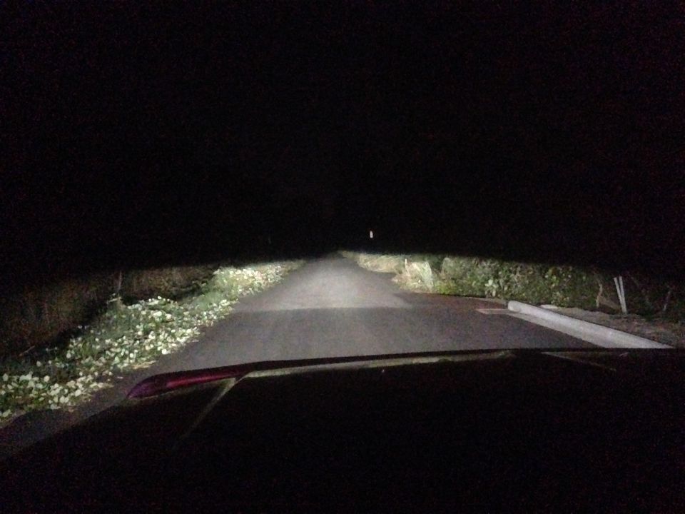 Interior view of a car driving on a dark road at night, headlights illuminating the path