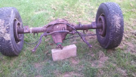 1979 Ford Bronco - A rusty rear axle assembly with tires is shown outdoors, supported by a single brick.