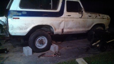 1979 Ford Bronco - This 1979 Ford Bronco is seen from the side, displaying a white body with a blue stripe and visible damage.