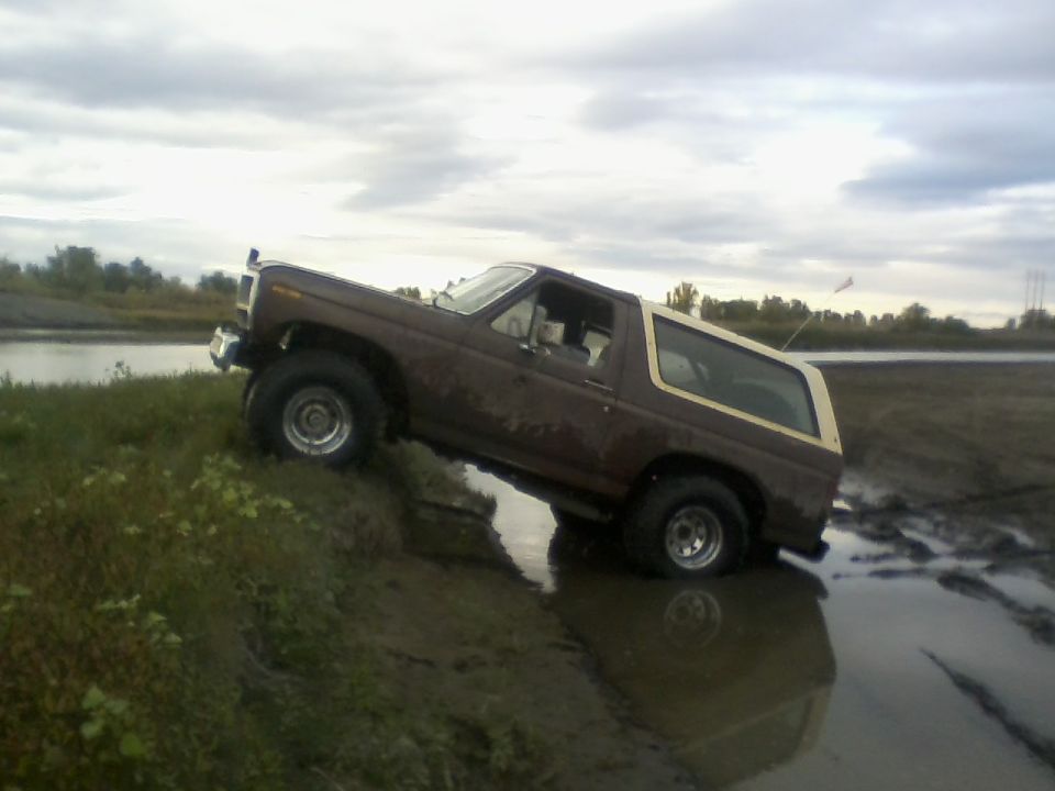 Brown 1980 Ford Bronco with a tan top driving through mud and water