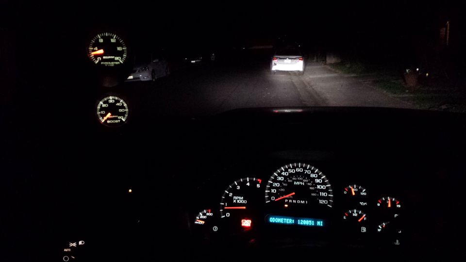 Dashboard with two gauges, speedometer, and odometer reading 120951 miles. Road ahead at night with headlights from another vehicle