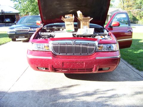 1999 Mercury Grand Marquis - Two Mercury Grand Marquis sedans are parked in a driveway, one with its hood open and new headlights visible.