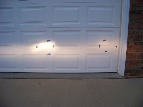 1999 Mercury Grand Marquis - Headlight beams are projected onto a garage door, with tape marking the edges of the light pattern.