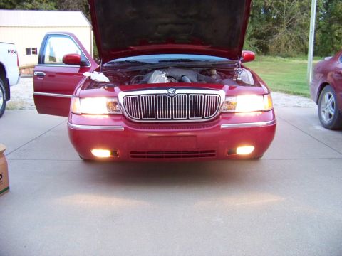 1999 Mercury Grand Marquis - Front view of a red 1999 Mercury Grand Marquis with its hood and driver door open, headlights illuminated.